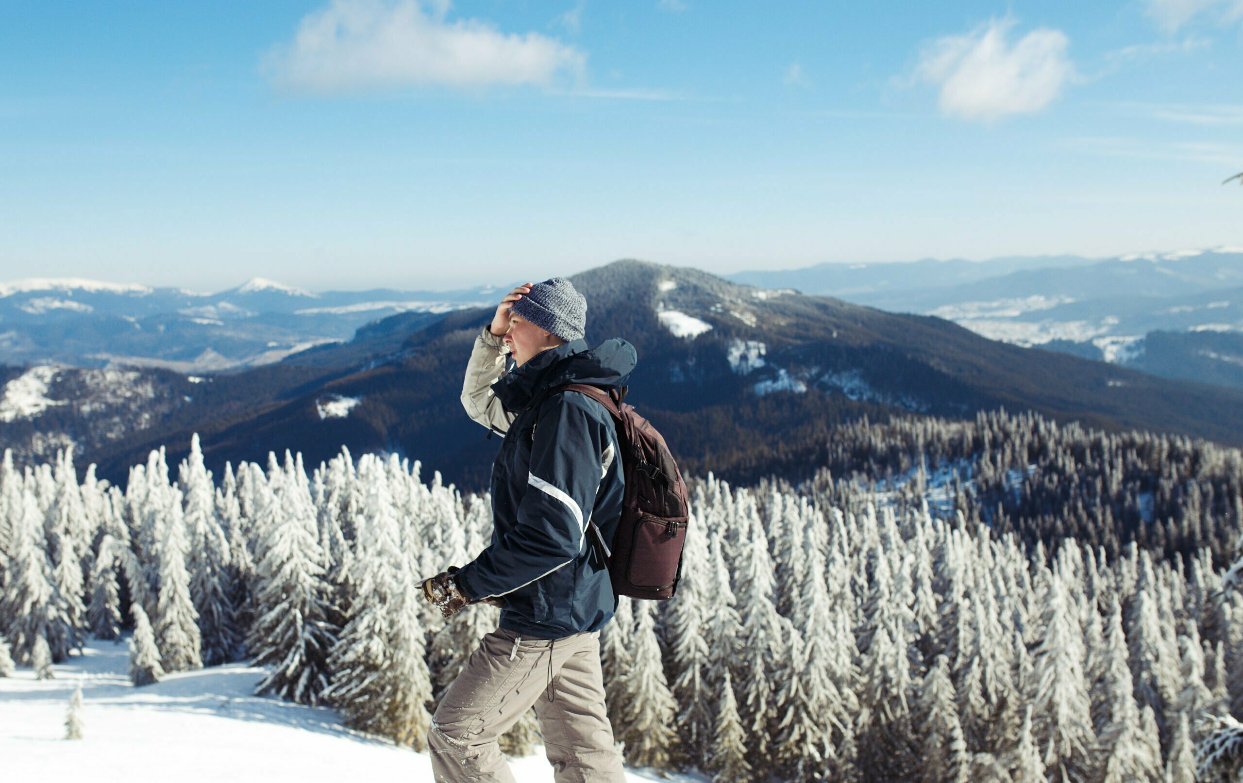 Man with backpack trekking in snowy mountains, cold weather hiking gear